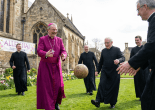 Clergymen in magenta and black robes playing with a vintage football outside a cathedral.
